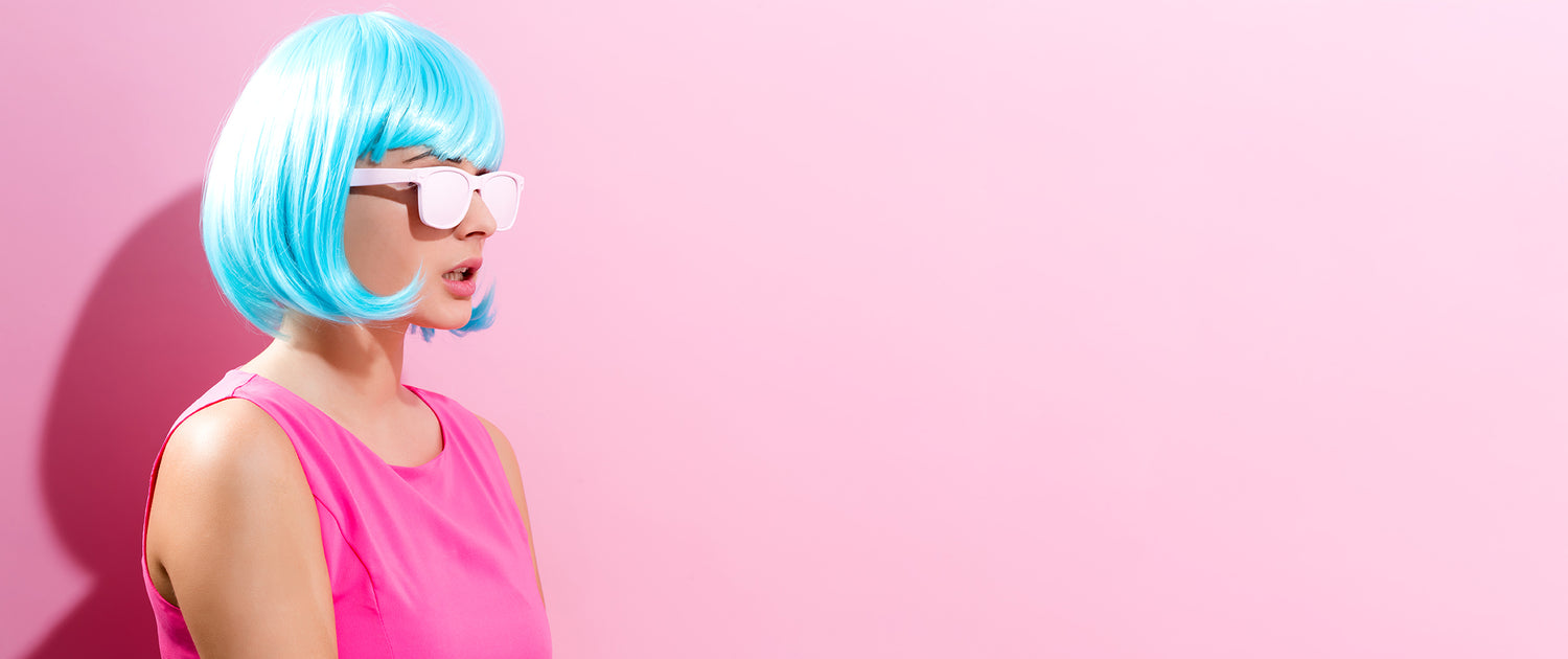 Woman in a pink tank top and light blue wig against a light pink backdrop